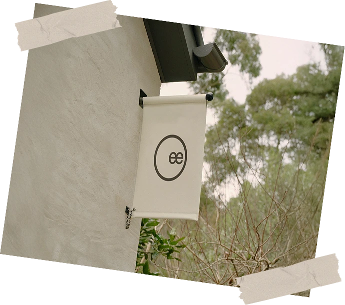 White banner with a black logo on a building exterior, surrounded by trees.